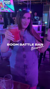 A group of friends enjoys a bottomless brunch at Boom Battle Bar, featuring cocktails, casual bar food like burgers and wings, and activities like shuffleboard. The video captures the upbeat, party atmosphere of the venue.