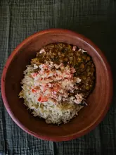 A top-down shot of a homemade bowl of dhal served with rice and a coconut sambal topping, presented in a rustic bowl on a dark textured cloth.