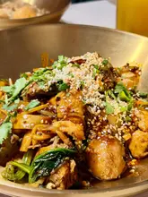 A close-up, top-down shot of a bowl of Malatang dry mix, featuring noodles, vegetables, and meat, topped with sesame seeds and cilantro.