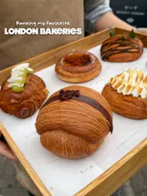 A high-quality, close-up shot of a tray filled with various artisan pastries, likely from a London bakery. The image is well-lit with natural light, highlighting the textures and glazes of the baked goods. The composition is clean, with a shallow depth of field that keeps the focus on the food while blurring the background.