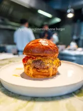 A high-quality, appetizing close-up shot of a pimento cheese burger, centered on a white plate with a blurred kitchen background.