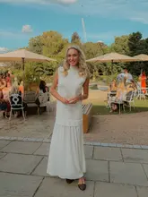 A high-quality portrait of a woman holding a glass of champagne at an outdoor event held at The Hurlingham Club. The image captures a sophisticated, social atmosphere with a shallow depth of field that keeps the focus on the subject while providing context of the event in the background.