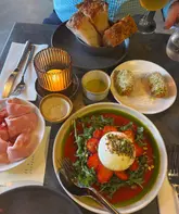 An overhead, flat-lay shot of a restaurant table featuring a burrata salad with strawberries, a plate of mortadella, and bread, captured in warm, atmospheric lighting.