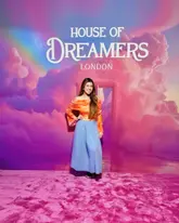 A promotional image featuring a creator posing in front of a branded backdrop at the House of Dreamers London immersive experience. The image is a standard influencer-style event photo.