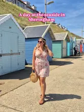 A bright, travel-focused lifestyle shot featuring a woman walking along the promenade in Sheringham, Norfolk, with iconic colourful beach huts in the background.