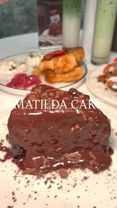 A short, high-quality video showcasing the 'Matilda Cake' at Haute Dolci in the Trafford Centre. The video features a slow-motion reveal of the cake as a metal ring is lifted, allowing chocolate sauce to drip over the sides, followed by a close-up of a fork cutting into the dessert.