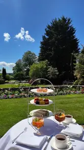 A serene, slow-paced video showcasing an afternoon tea service set in a lush garden. The footage highlights the tiered stand with sandwiches, macarons, and tarts, accompanied by Pimm's, emphasizing a quintessentially British summer atmosphere.