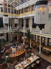 A high-angle, wide-shot photograph of the atrium at the NoMad London, showcasing the impressive architectural design, glass roof, and dining setup for afternoon tea.