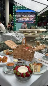 A short, aesthetic reel showcasing a Wimbledon-themed afternoon tea served in a picnic basket at the Ham Yard Hotel, featuring close-ups of various pastries, sandwiches, and scones in an outdoor courtyard setting.
