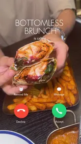 A fast-paced, visually engaging reel promoting a bottomless brunch at an Indian restaurant. The video uses a creative 'incoming call' interface overlay to frame the content, transitioning quickly between shots of cocktails, various Indian dishes like butter chicken and wraps, and sides, effectively highlighting the menu variety.