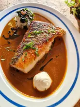 A top-down shot of a seared hake fillet served in a rich masala sauce with a dollop of smoked yoghurt and a side of pickled cabbage, captured on a rustic wooden table.