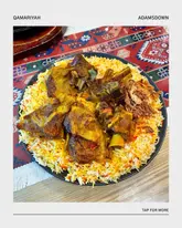 A top-down, brightly lit shot of a plate of Lamb Mandi served on a patterned tablecloth, showcasing the generous portion of slow-cooked meat and spiced rice.