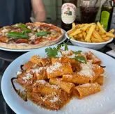 A casual dining shot featuring a plate of pasta in the foreground, with a pizza and fries in the background, capturing a shared meal experience.