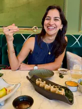A high-quality, engaging lifestyle shot featuring a diner enjoying sushi in an elegant, upscale restaurant setting. The composition is balanced, with the subject's genuine expression drawing the viewer in, while the table setting provides context for the dining experience.