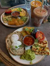 A high-quality, overhead flat-lay photograph of two vegetarian brunch plates and two juices on a rustic table, showcasing a well-presented meal at a cafe.