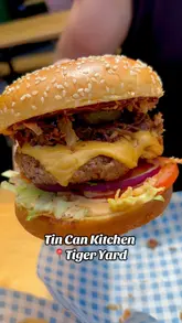 A couple visits Tin Can Kitchen at Tiger Yard, showcasing their burgers and loaded fries in a casual outdoor setting.