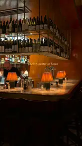A short, moody montage showcasing the interior, bar, and food offerings of Bosco, an Italian restaurant. The video highlights the atmosphere and specific dishes like arancini, pizza, and zucchini fritti.