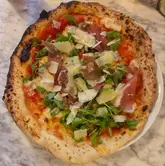 A top-down, overhead shot of a Neapolitan-style pizza topped with prosciutto, rocket, and shaved cheese, served on a marble table.