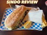 A straightforward, top-down photograph of a sandwich and fries served on a tray with blue and white checkered paper, likely taken in a pub setting. The image includes a text overlay indicating it is a review.