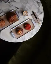 A beautifully composed, moody overhead shot of a selection of pastries and a coffee served on a marble table, creating an inviting and aesthetic cafe atmosphere.