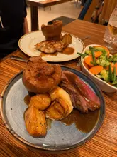 A standard, casual photograph of a Sunday roast dinner served at a hotel restaurant. The image captures two plates of food and a side of vegetables on a wooden table, typical of a relaxed weekend meal.