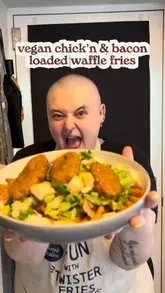 A home cooking tutorial demonstrating how to prepare a vegan loaded waffle fries dish using store-bought ingredients. The creator shows the process of air-frying the fries and vegan chicken, chopping salad ingredients, and assembling the final dish in a bowl.