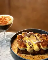 A high-quality, professional food photography shot featuring a decadent Tiramisu French Toast and an Espresso Martini, likely taken in a restaurant setting.