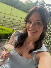 A high-quality, personal selfie taken at an outdoor venue featuring a glass of wine and a scenic deer park in the background, capturing a celebratory atmosphere.