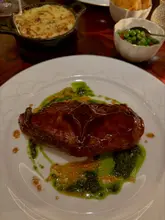 A high-quality, moody shot of a lamb chop main course served with a side of potato dauphinoise and peas, captured in a fine-dining restaurant setting.