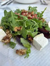 A close-up, overhead shot of a beetroot, goat's cheese, and walnut salad served on a white plate, likely taken in a restaurant setting.