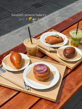 A high-angle shot of various pastries and drinks arranged on wooden trays on an outdoor table, captured in bright, direct sunlight.