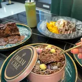 A flat-lay style shot of a dessert spread featuring a 'Dream Cake' in a tin, a chocolate cake, a fruit platter, and various drinks, showcasing a casual dessert venue.
