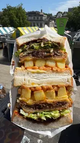 A short video review of the 'Lanes Fayre Special' sandwich from The Bodega, featuring a close-up of the ingredients including a steak bake, chips, beans, and cheese, set against a market backdrop.