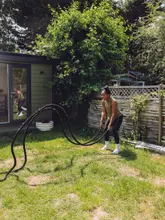 A woman performing battle rope exercises in her garden, marking the 14th anniversary of her fitness business.