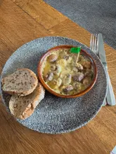 A top-down shot of a bowl of creamy mushrooms served with two slices of bread, presented on a speckled plate on a wooden table.