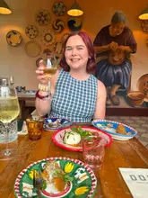 A bright, inviting lifestyle shot of a diner enjoying a meal at a restaurant, featuring a glass of wine and plates of food on a rustic table, with a decorated wall in the background.