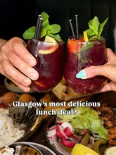 A close-up, eye-level shot of two people holding glasses of sangria in a toast, with a spread of Middle Eastern small plates visible in the blurred background. The image is used to promote a lunch deal at a restaurant.