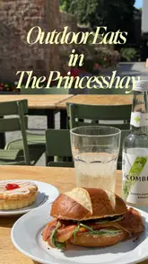 A creator visits Chandos Deli in Princesshay, Exeter, to enjoy an outdoor breakfast. The video showcases the deli's exterior, its food display, and the creator enjoying a bacon roll, a cherry bakewell, and an elderflower drink in the sunshine.