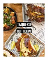 A high-quality, overhead flat-lay shot of a table spread at Taquero in Nottingham, showcasing various dishes including tacos and crispy pork belly alongside the restaurant's menu.