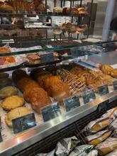 A close-up shot of a bakery display case filled with a variety of pastries, including croissants, pain au chocolat, and apple pies, with price labels clearly visible.