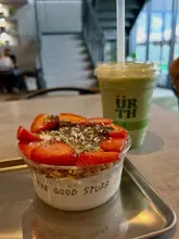 A casual, user-generated style photo featuring a yogurt bowl and a matcha latte on a metal tray, likely taken inside a cafe.
