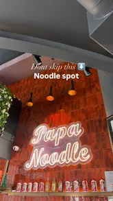 A food review video featuring a visit to Papa Noodle, showcasing various dishes including beef soup noodles, dry noodles, chicken balls, veggie gyoza, and chicken thigh skewers. The creator provides commentary on the food quality and mentions a discount app.
