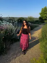 A lifestyle photograph featuring a woman walking along a gravel path in a garden setting, holding a glass of wine, captured during a summer media showcase event.