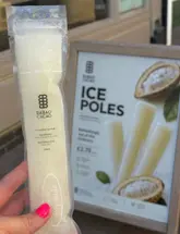 A close-up, hand-held shot of a cacaofruit ice pole, with a promotional sign for the product visible in the blurred background.