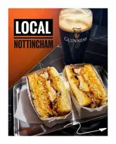 A high-contrast, appetizing shot of a fried chicken sandwich and a pint of Guinness, set against a vibrant orange wall, effectively showcasing the casual, trendy atmosphere of the venue.