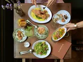 A high-quality, overhead flat-lay photograph of a lunch spread at Willetts, featuring various dishes including fish, salad, and cocktails, presented on a wooden table with elegant tableware.