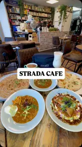 A promotional reel for Strada Cafe featuring a spread of Desi-style dishes including Lamb Nihari, Samosa Chaat, Chana & Paratha, Lassi, and Chai. The video uses a mix of static table shots and close-up handheld shots of food interaction to highlight the menu.