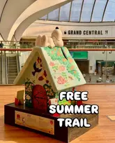 A promotional image for the 'Snoopy in Birmingham' art trail, featuring a painted Snoopy sculpture on top of a doghouse located inside the Grand Central shopping centre. The image includes text overlay promoting the free summer activity.