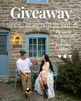 A promotional image for a giveaway featuring a couple sitting outside a stone cottage in the Yorkshire Dales, holding wine glasses. The image uses a soft, natural aesthetic to convey a luxury, relaxing countryside escape.