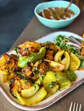 A close-up, eye-level shot of a Chicken Shashlik dish featuring grilled chicken, peppers, and onions, served with a side salad and a bowl of curry in the background.